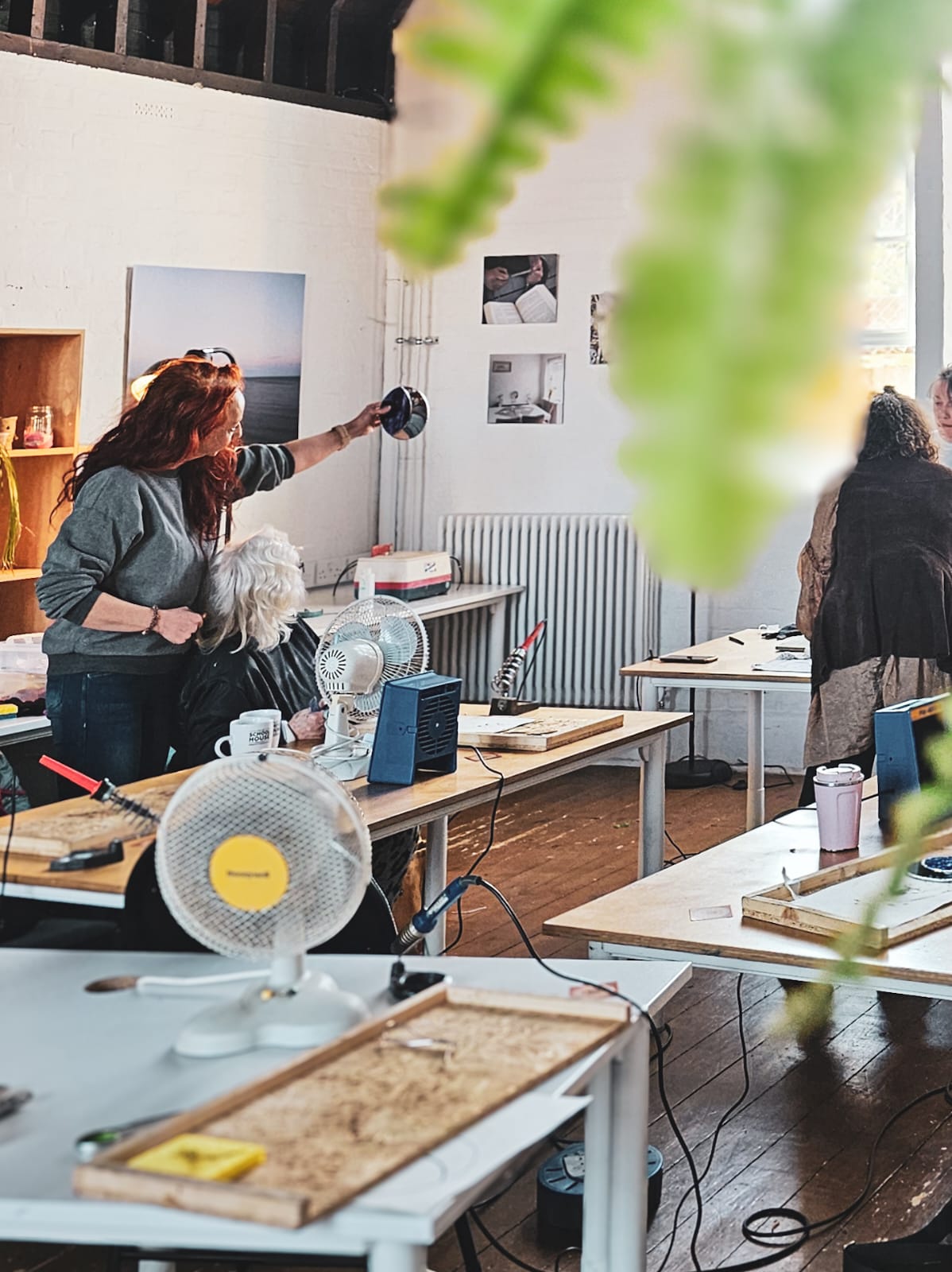 Classroom setting with people and tools on tables, two workshop attendees admire their finished stained glass creation in the light for the first time.