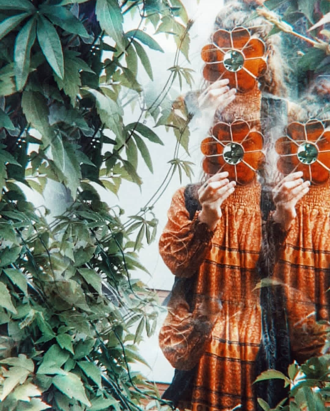 Photo of the founding artist Yiscah Rosemary holding a stained glass flower in front of her face, surrounded by greenery.