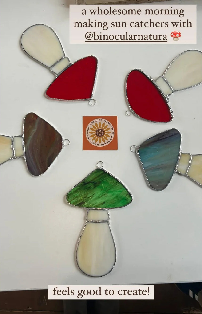 Colorful stained glass mushroom sun catchers made at a workshop on a white surface with business card in center.